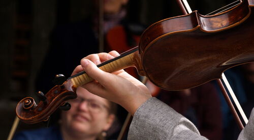 Nahaufnahme einer Geige, die von einer Person gespielt wird, sichtbar sind Hände, Instrument und Bogen.