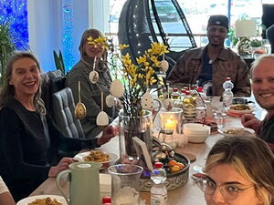 Langer gedeckte Tisch mit 12 Personen. Gemeinsames Abendessen. Alle lächeln in die Kamera.