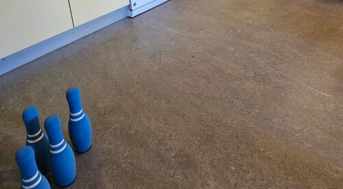 Küchenzeile.   Daneben stehen blaue Kegel. Ein ältere Mann am rechten Bildrand kullert ein Ball in Richtung Kegel.