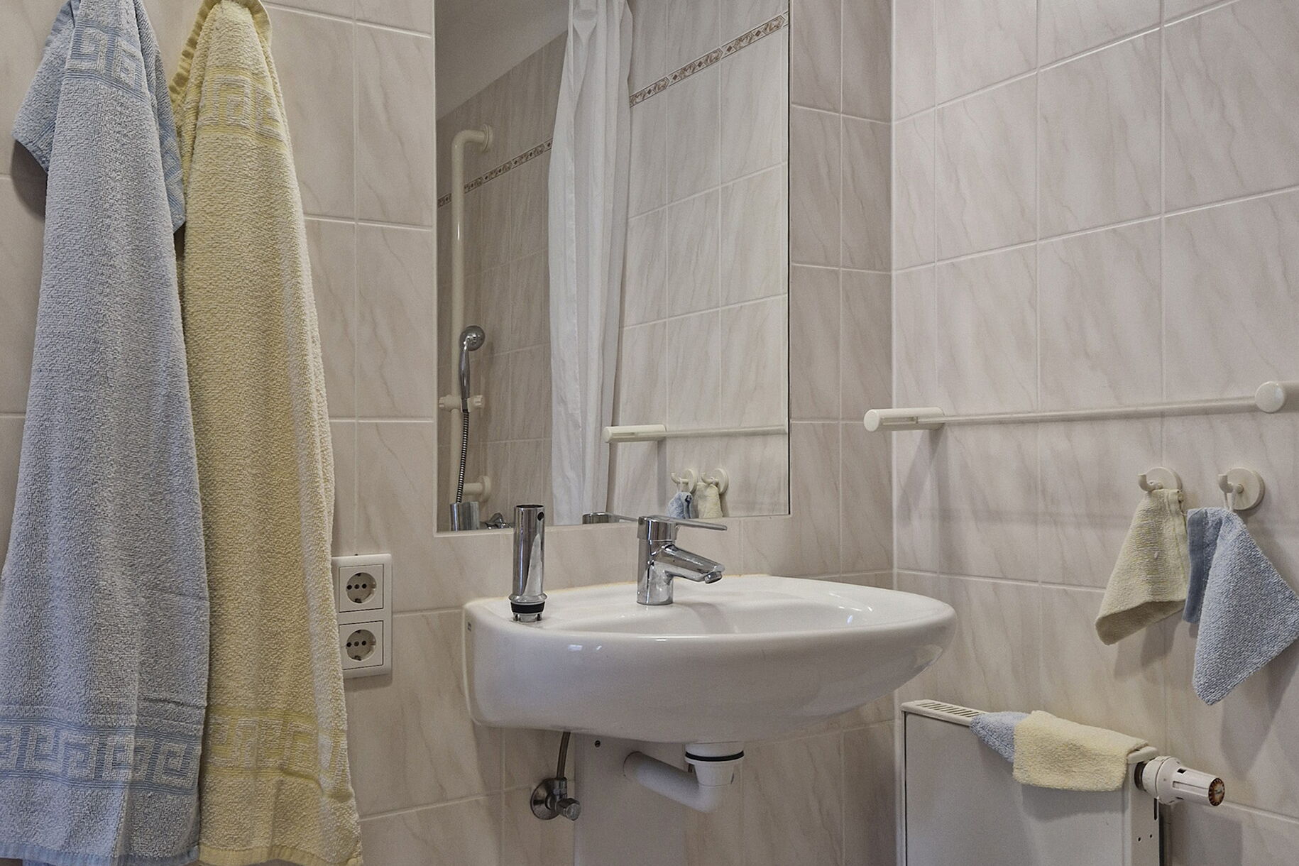 Badezimmer. Waschbecken, großer Spiegel darüber. Links daneben zwei Handtücher.