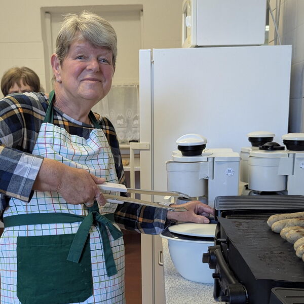 In einer Küche, Frau mit Grillschürze und Grillzange in der rechten Hand an den Bratwürsten.