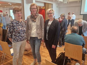 Großer Raum. Drei Frauen stehen Portrait. Sie lächeln in die Kamera.