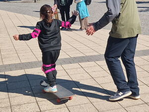 Mädchen auf einem Skateboard.  Mann läuft nebenher und passt auf.