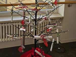 Weihnachtliches Tannenbaum-Gerippe mit Lichterkette und vielen gerollten Wunschzetteln. Drinnen steht vor einem Fenster.