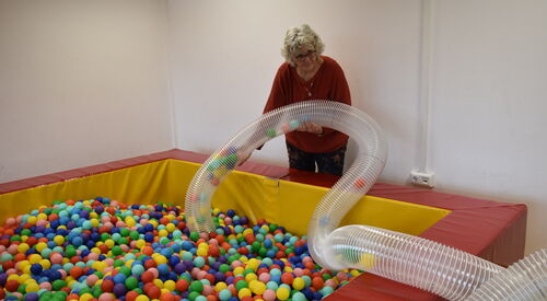 Aus einem Bällebad werden viele bunte Bällen gesaugt. Eine Frau hält den Schlauch durch den die Bälle kullern fest.