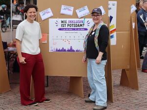 2 Frauen vor einer Stellwand mit Plakat. Die Frage: Wie inklusiv ist Potsdam?   Darunter ein Strahl von 1 bis 10.