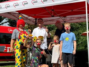 AWO Pavillon. Clown, eine Clownin, ein Mädchen und ein Junge, die Kinder mit roter Clownsnase. Clownin mit roter Nase und einem kurzen farbenfrohen Kleid hockt ganz vorn. großer Clown mit roter Perücke und gelber Latzhose mit bunten Tupfen.