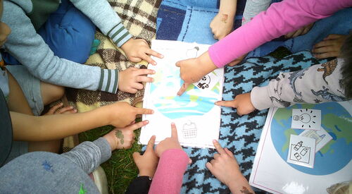Mehrere Kinderfinger halten das Bild mit der fröhlichen Erde/Welt fest oder tippen darauf.