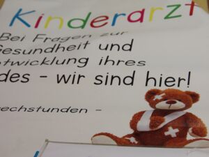 Ein Plakat auf dem steht: Bei Fragen zur Gesundheit und Entwicklung ihres Kindes - wir sind da.    Ein Teddy mit Pflastern und Armbinde ist auf dem Plakat abgebildet.