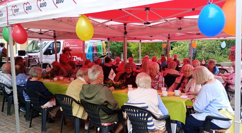 Pavillons mit Luftballons geschmückt. Menschen sitzen bei Kaffee und Kuchen darunter an langen Tischen.