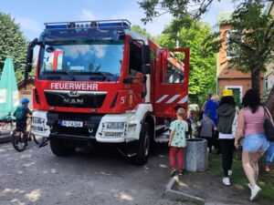 Einsatzfahrzeug der Feuerwehr Potsdam von vorne. Kinder und Erwachsene sehen es sich an.