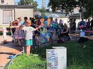 Draußen bei warmen Wetter, Sonne scheint. Kinder und Erwachsene machen Riesen-Seifenblasen.