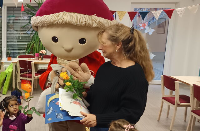 Der Sandmann in Lebensgröße nimmt Karten, Bilder und Blumen zum Geburtstag entgegen. Frau übergibt ihm alles. Kinder stehen um ihn rum.