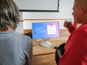 Zwei Personen vor einem Monitor mmit Maus, darauf ein Mitmach-Quiz.