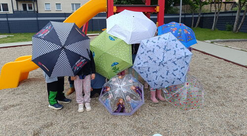 Kinder auf einen Spielplatz vor einer Rutsche. Viele bunte Regenschirme verdecken die Kinder.