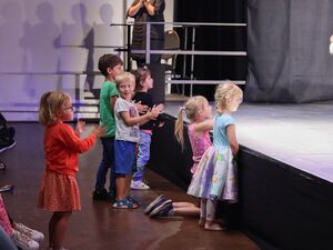 6 Kinder, Mädchen und Jungen vorn am Bühnenrand applaudieren.