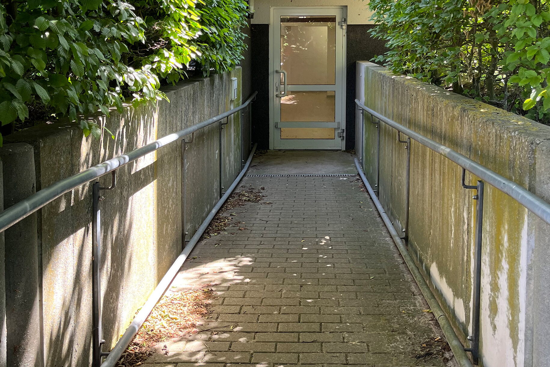 Eine Rampe mit Geländer auf beiden Seiten führt hinab zu einer Tür.