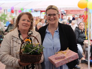2 Frauen, eine mit Blumenkörbchen,  die andere mit Geschenken. Beide lächeln in die Kamera.