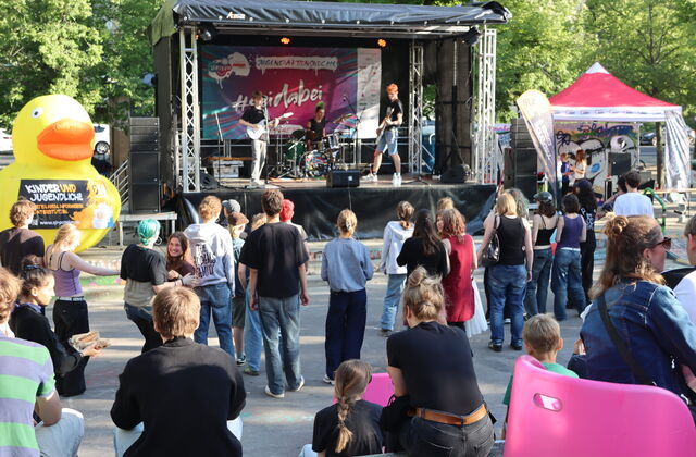 Auf der Bühne, Band bestehend aus 3 Personen. Vor der Bühne begeistertes tanzende Publikum.