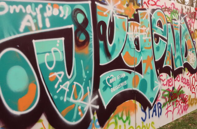 Eine Mauer / Wand, voll gesprayt mit Worten. Das grüößte ist das Wort Jugend - darin das AWO Logo - AWO gegen Rassismus.