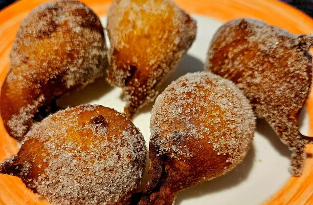 Orangenbälle. Quarkbällchen ähnlich mit Zucker bestreut. Liegen auf einem Teller mit Orangenen Rand.