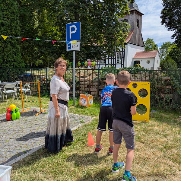 Zwei Kinder beim Wurfspiel. Eine gelbe Platte mit Löchern ist aufgestellt, die Kinder werfen.