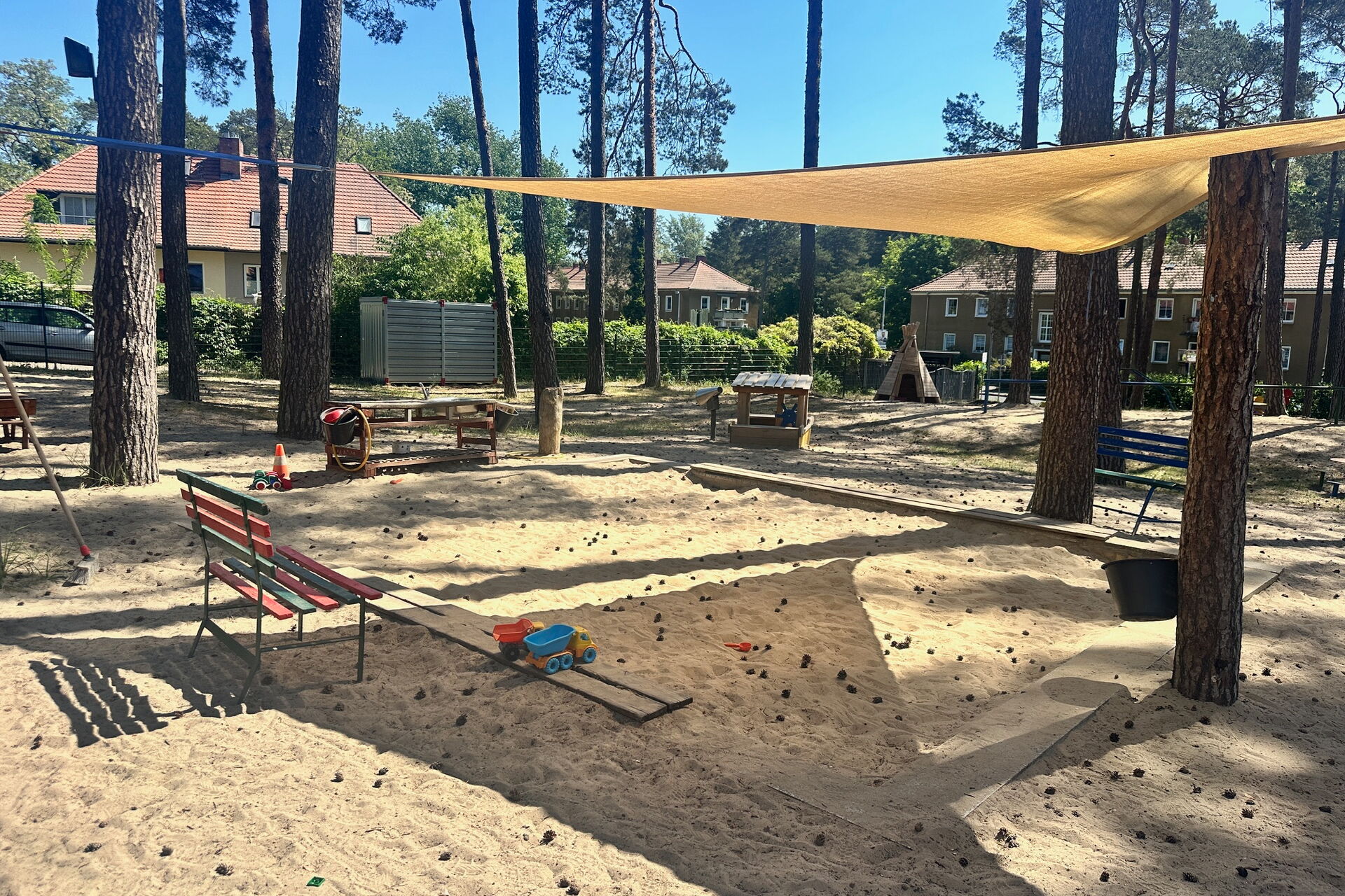 Sandkasten überdacht mit gelben Sonnensegel das an umstehenden Bäumen befestigt ist.