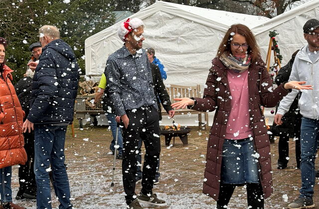 Menschen freuen sich über Kunstschneegestöber. Weiße Flocken am Boden.