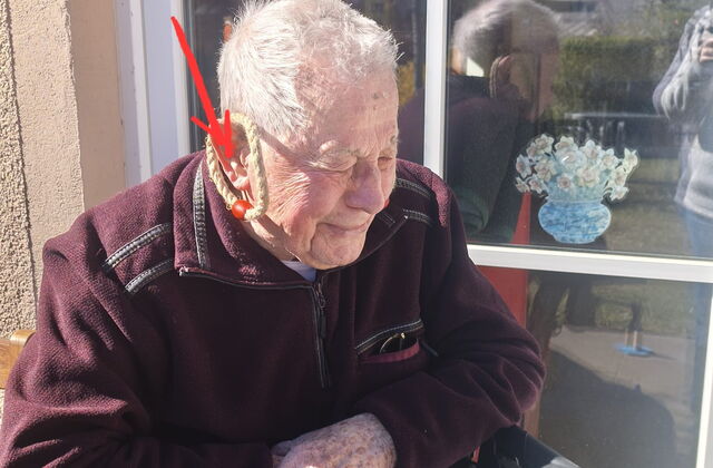 Alter Mann sitzt aus seinem Rollator draußen in der Sonne.