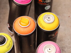 9 verschieden farbige Spraydosen stehen auf dem Boden.