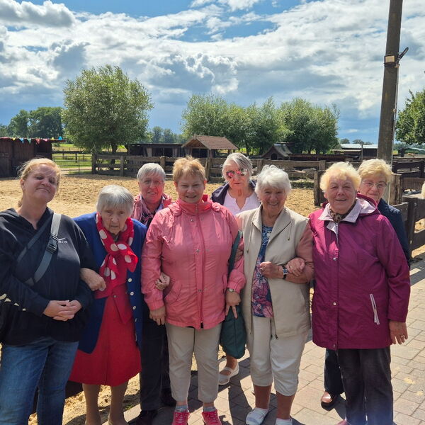 Gruppenfoto: 8 ältere Frauen vor einer Pferdekoppel. Fröhlich bei sonnigen Wetter.