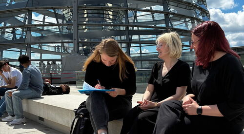 In der Sonne auf dem Doch vor der großen Glaskuppel. 3 Frauen sitzen dort und eine fülllt die Unterschriften Liste aus.