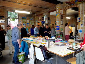 Atelier. Großer Raum mit Bildern an den Wenden. Menschen schauen sich die Kunst an.