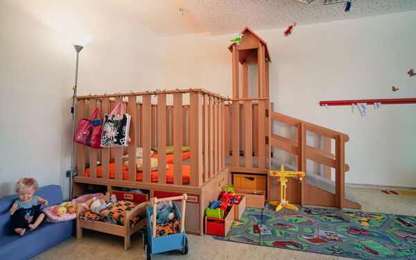 Spielzimmer. Mit Puppen, Puppenwagen, Puppenbett, ein Kinder-Straßen-Teppich und ein Kindergarten-Hochebene mit Matratzen und Kissen.