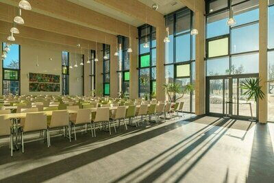 Großer Saal, mit vielen Tischen und Stühlen. Große Fenster die viel Licht herein lassen. Hinten ist eine große Glastür die Sonne scheint in den Raum.