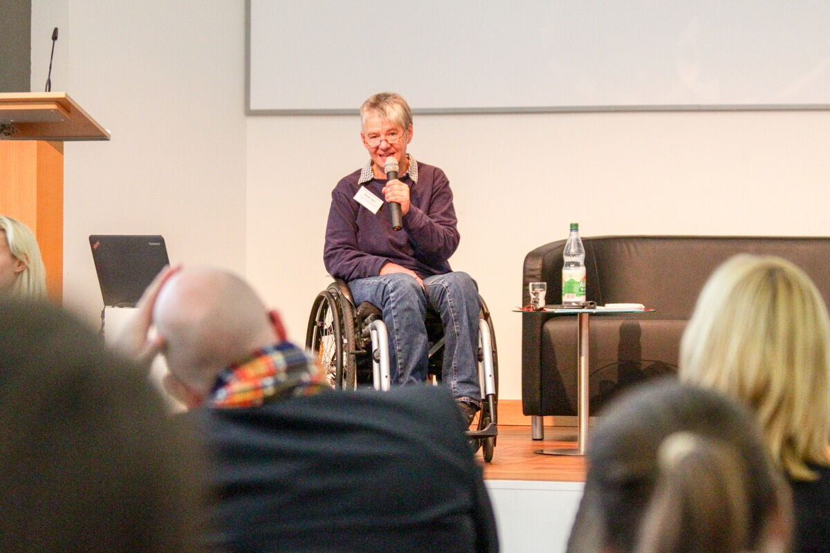 Fr. Dr. Arnade von der ISL Berlin stellt dem Fachtagspublikum neben dem Rednerpult vom Rollstuhl aus das Mentorenprojekt  Job-Win-Win vor.