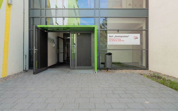 Eingang. Verglast. Große Türen. An der Scheibe rechts ein großes Schild: Hort Havelsprotten.