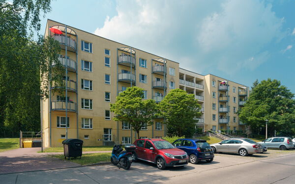 Großes Wohnhaus mit hellgelber Fassade und davor parkenden Autos.
