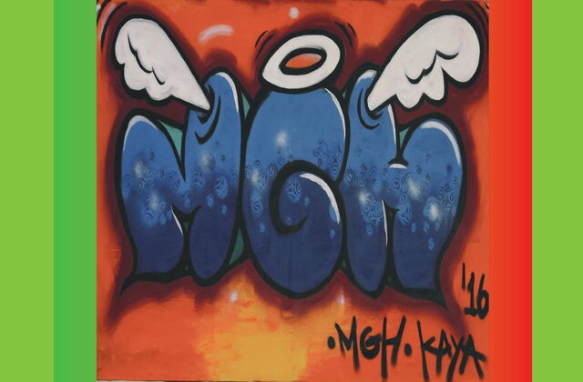 Ein Graffiti mit grünen Rahmen. Die Großbuchstaben MGH in blau auf orangenen Hintergrund. Die Buchstaben M und H haben oben weiße Engelflügel und das G einen weißen Heiligenschein.