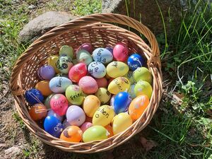 Körbchen mit bunt gefärbten und bemalten Ostereiern. Das Körbchen steht draußen an einem Stein. Die Sonne scheint.