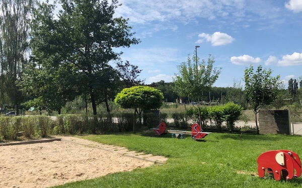 Spielplatz, Sandkasten, auf dem Rasen eine Wippe und ein kleiner Elefant auf dem man reiten kann.