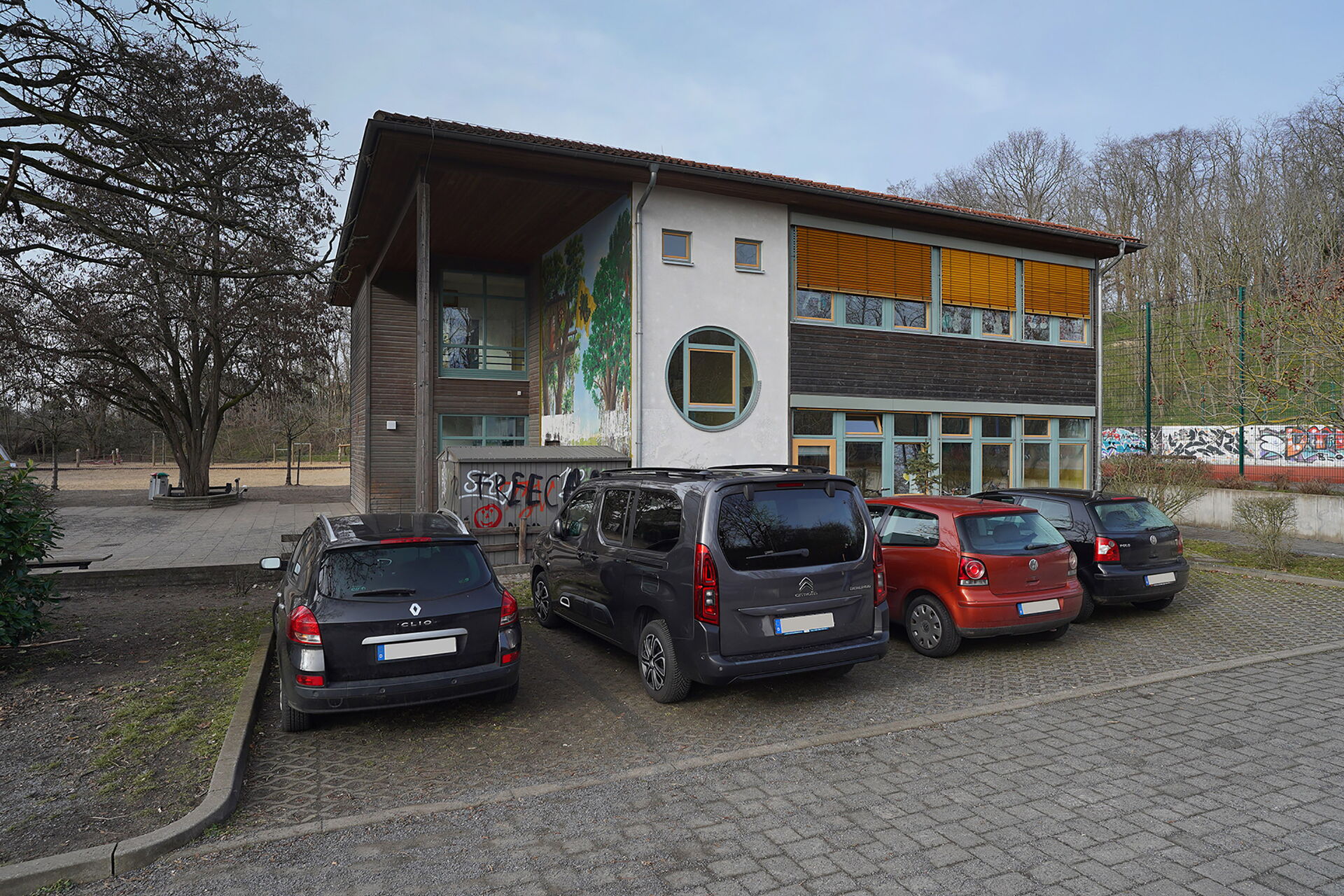 4 parkende Autos vor dem Gebäude. Gebäude ist ein kleiner moderne Bau mit zwei Stockwerken.