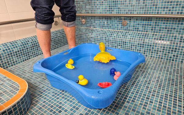 blaues Kleinkindbecken in gefliestem Großbecken. Im Becken schwimmen gelbe Enten.