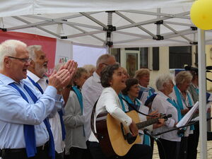 Gemischter Chor. Eine Person mit Gitarre die anderen Klatschen und Singen.