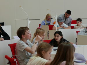 Kinder und Erwachsene im Plenarsaal an den Tischen.