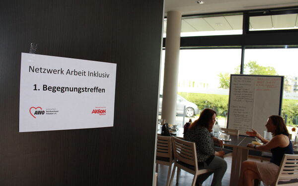 Blick in einen Raum. Zwei Frauen unterhalten sich angeregt. Sie sitzen an einem Tisch.