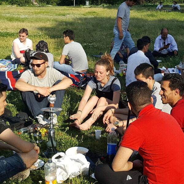 Picknick auf der Freundschaftsinsel. Menschen sitzen auf Decken oder auf der Wiese mit Getränken und Essen.