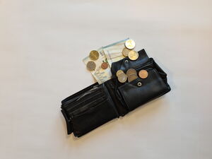 Eine geöffnete schwarze Geldbörse liegt auf einer hellen Fläche, darin und daneben liegen mehrere Euro-Münzen.