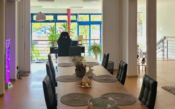 Esszimmer mit dem Wohnbereich verbunden. Langer Holztisch mit 8 schwarzen Stühlen und Tischdeko.