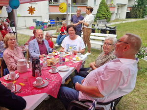 Fest. Menschen sitzen an Kaffeetafeln unter geschmückten Pavillons.